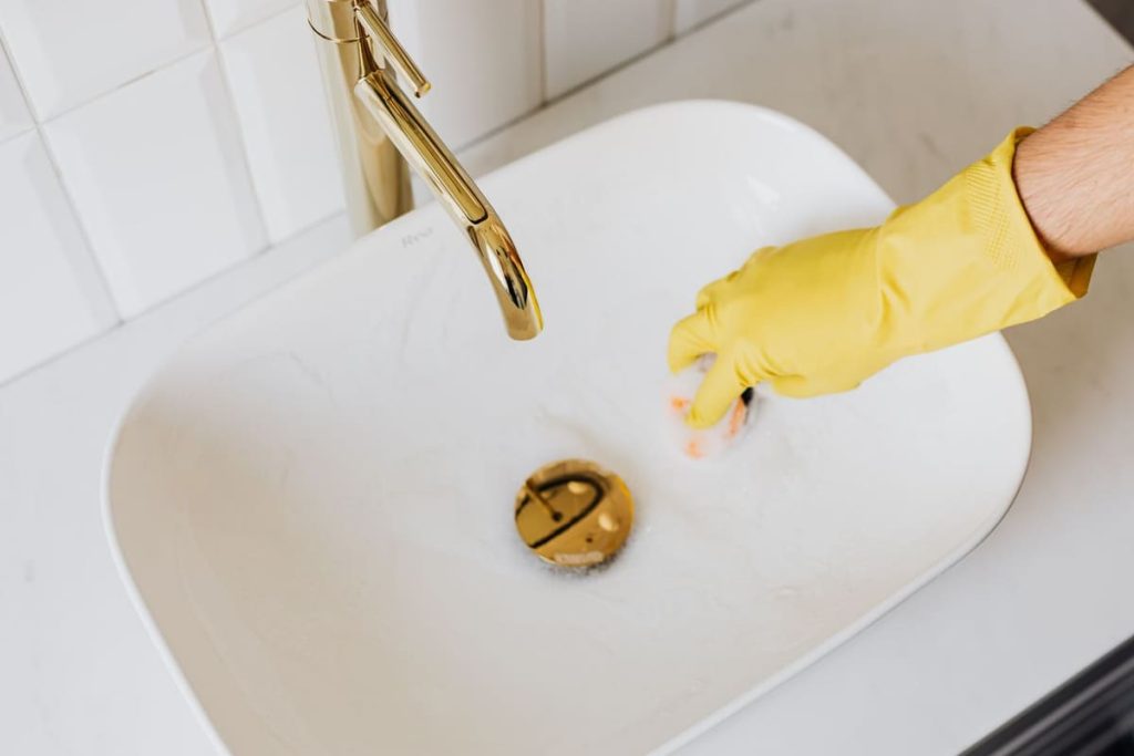 Gloved hand cleaning the drain of a bathroom sink