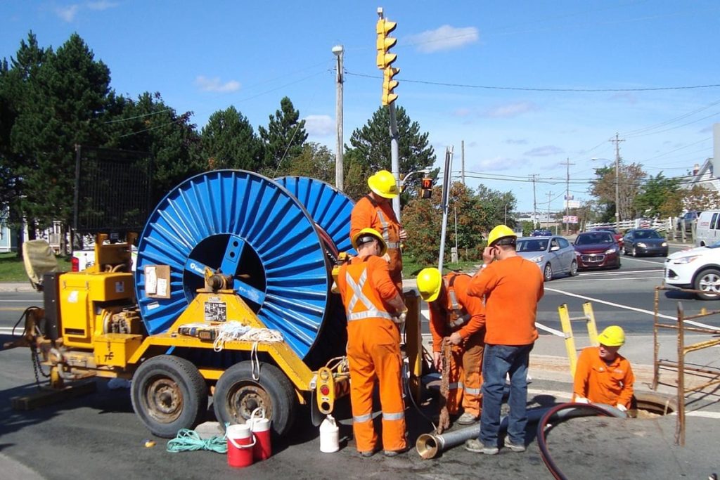 Crew feeding a jetting hose from a reel into a street sewer