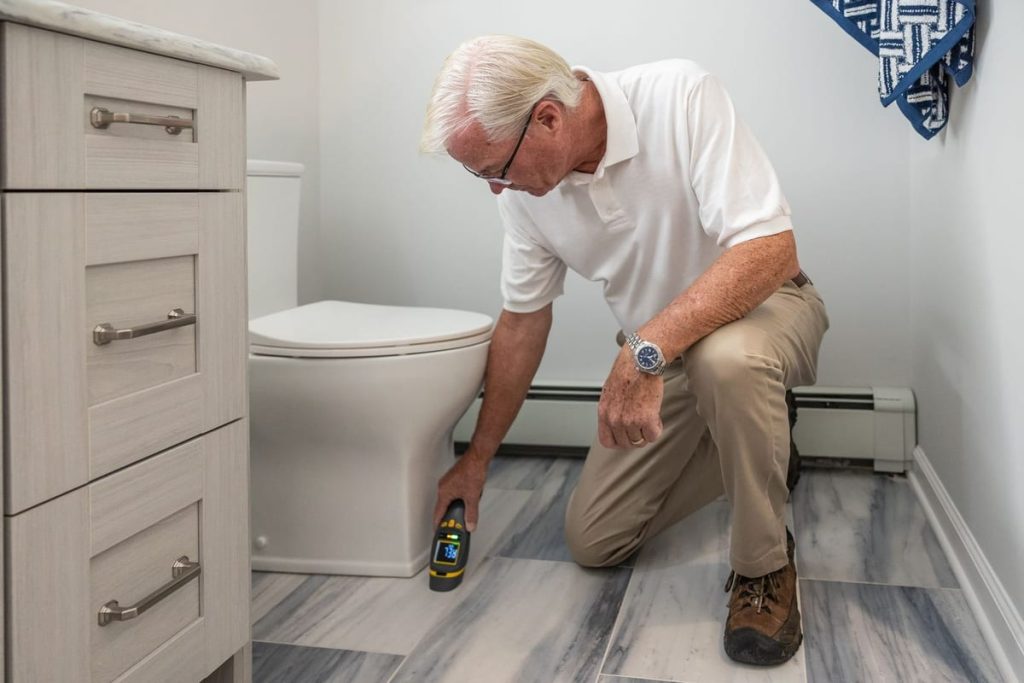 Man checking the plumbing beside a toilet with a handheld tester