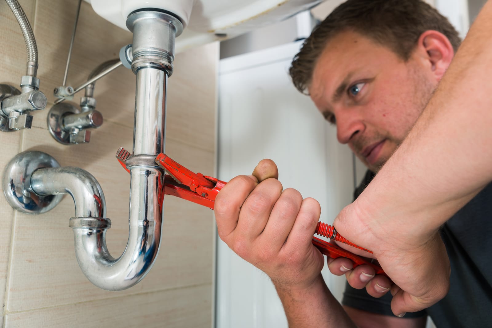 Plumber tightening a sink drain trap with pliers