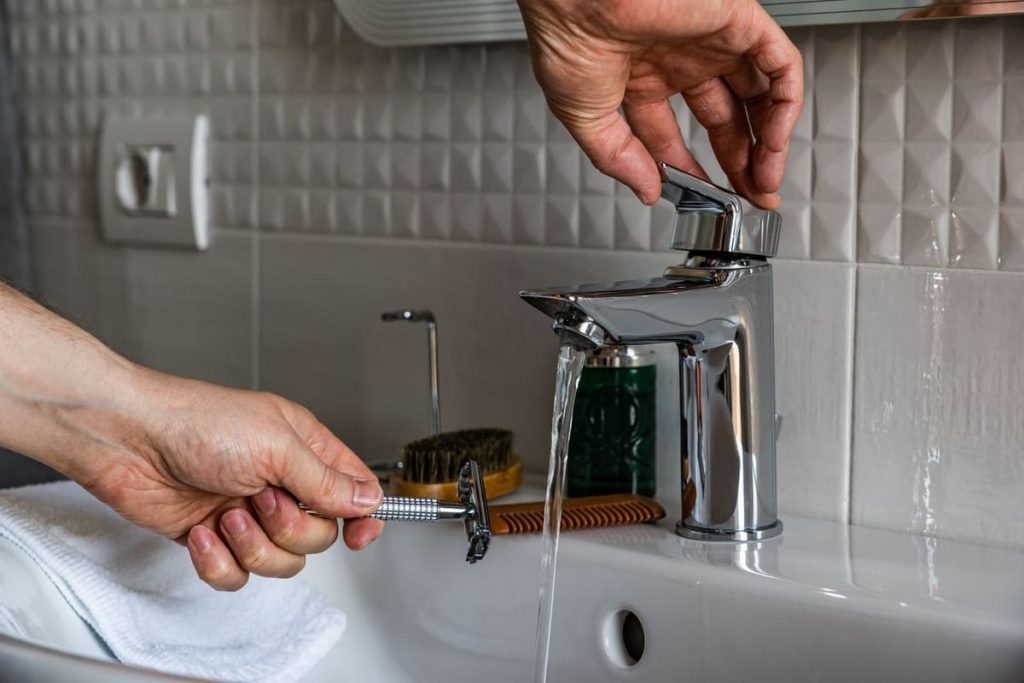 Hands repairing a bathroom faucet with a tool