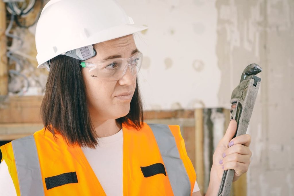 Plumber in a hard hat and safety glasses holding a pipe wrench