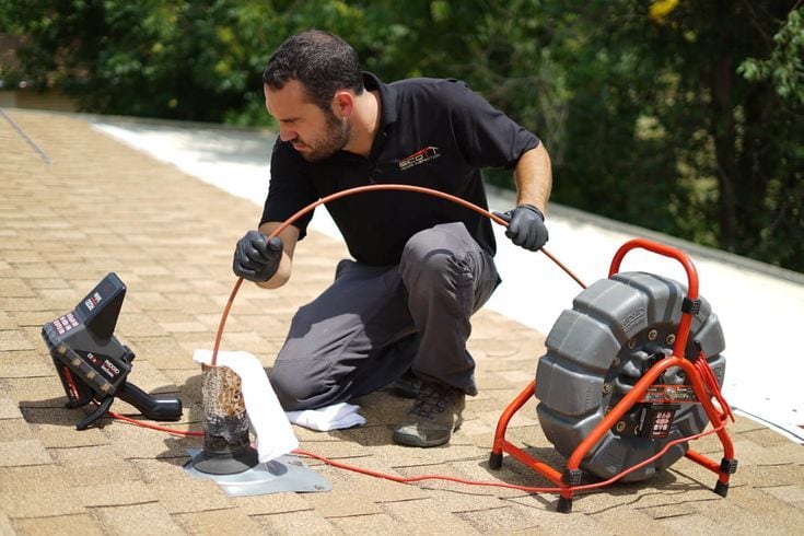 Technician feeding a sewer camera cable into a roof vent