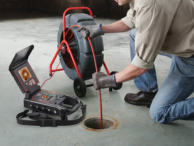 Plumber guiding a camera cable from a reel into a floor drain