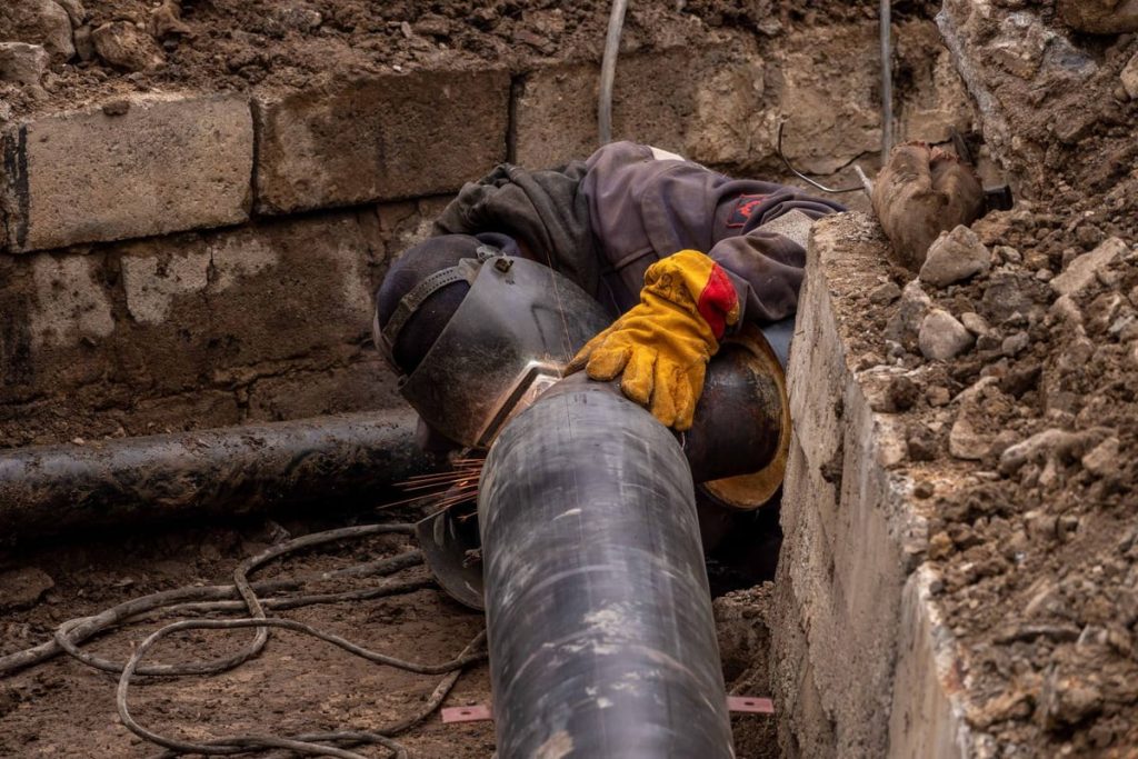 Worker repairing a large pipe in a street trench