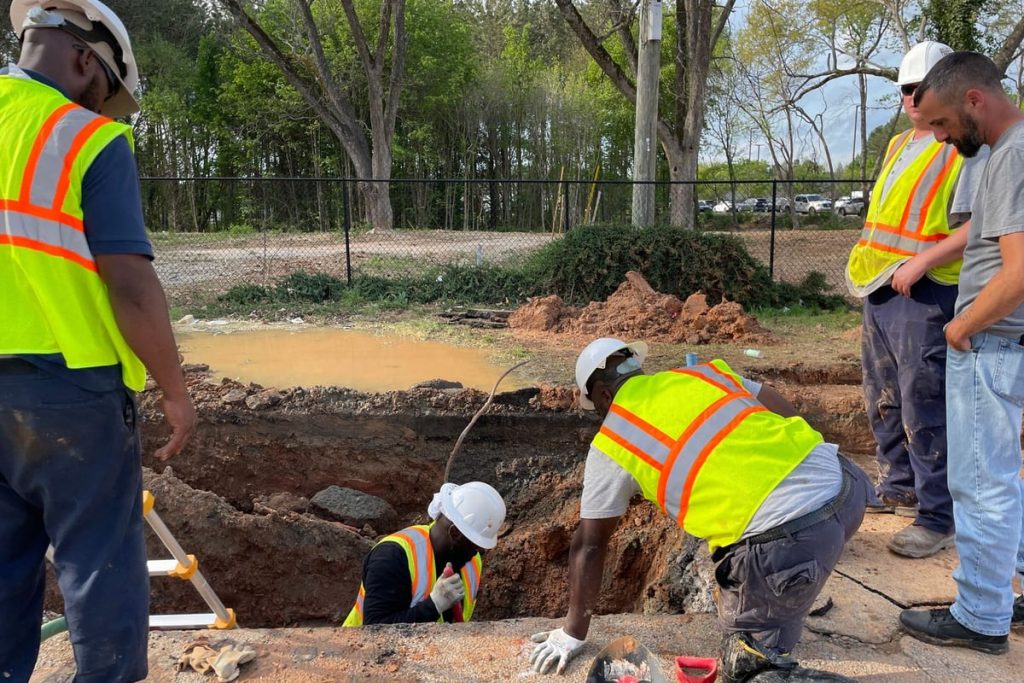 Crew inspecting a flooded excavation over a broken pipe