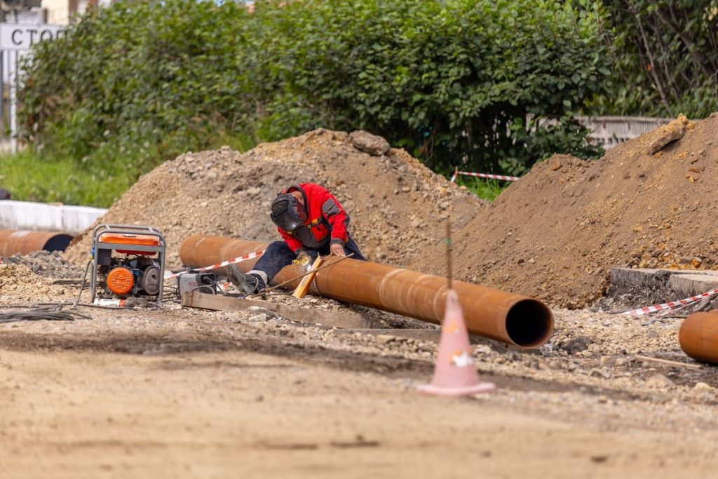 Worker joining a length of pipe beside an excavation