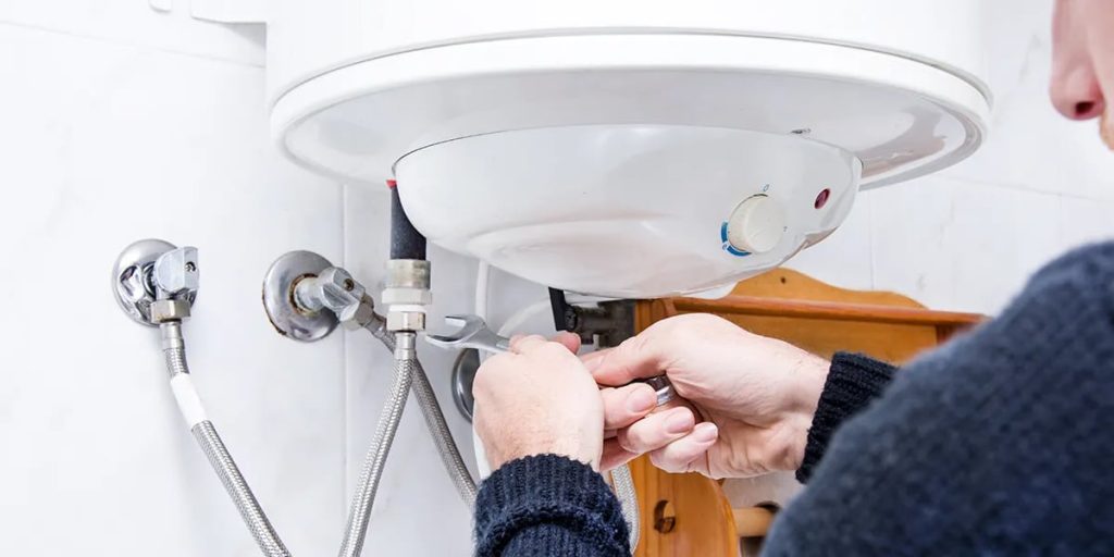 Hands connecting pipes beneath a water heater